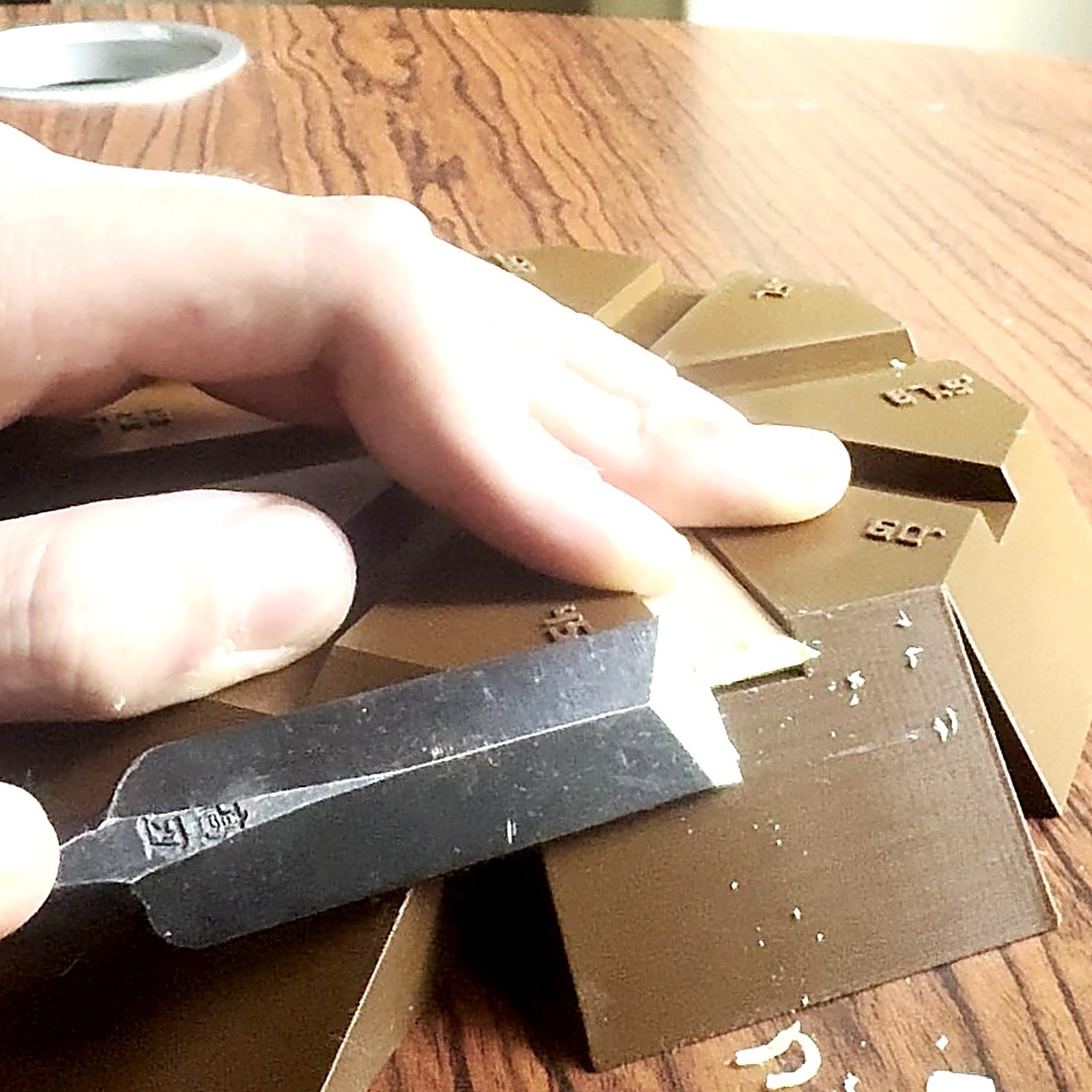 A Japanese chisel paring the end of a kumiko strip against the star jig, with shavings on the bench